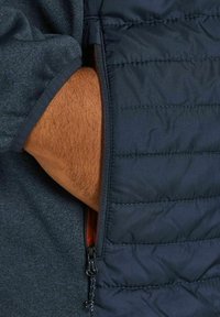 Marinblå zip-väst med kviltad textur och kontrasterande orange foder; tyget har en slät yta och integrerade fickdetaljer.