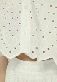 Witte geborduurde blouse met een geschulpte zoom, voorzien van uitsnijdingen en halve mouwen, knoopsluiting aan de voorkant, gestructureerde stof.
