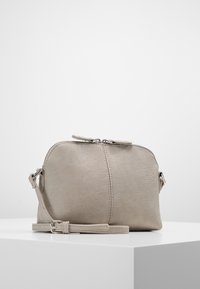 Borsa a tracolla in pelle grigia chiara con forma arrotondata, chiusura superiore con zip, tracolla piatta e un sottile dettaglio testurizzato sulla superficie.