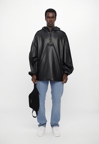 Must black, ülepaisutatud vinüülpullover neljanda tõmbluku ja ees oleva taskuga. Kandmine helesiniste teksade peal, koos musta õlapaelaga kotiga.