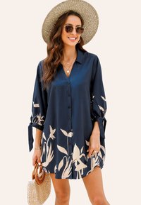 Camisa de botones azul marino hecha de material sedoso, con ligeros patrones florales, mangas enrolladas con lazos y un corte relajado.