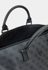 Borsa a tracolla grigia con motivo e dettagli in pelle nera, manici doppi e chiusura con zip. L'interno presenta una fodera nera con il logo "GUESS".