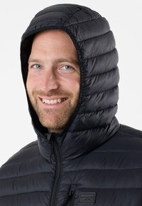 Zwarte, puffy, capuchonjack met een gewatteerde structuur. Voorzien van een volledige rits en een klein logo op de borst. Gemaakt van lichtgewicht materiaal.
