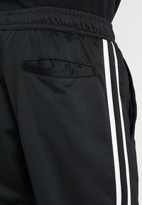 Svarta träningsbyxor med vita sidosträck och ett elastiskt midjeband, med en slitsbackficka.