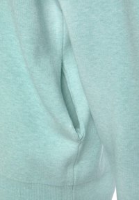 Mintgrüner Sweatshirtstoff mit weicher Textur; verfügt über eine Seitentasche und einen gerippten Saum. Schlichtes Design ohne sichtbare Markenkennzeichnung oder Muster.