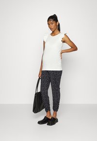 Top branco sem mangas com ombreiras franzidas, combinado com calças de jogger pretas com bolinhas. Uma bolsa preta e tamancos completam o conjunto.