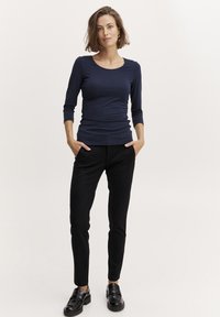 Top ajustat cu mânecă lungă de culoare bleumarin, asortat cu pantaloni negri skinny și mocasini negri. Material moale cu o textură netedă și guler rotund clasic.