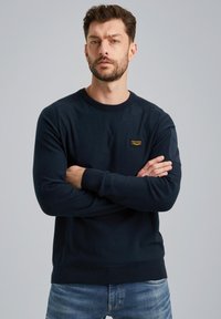 Maritieme crewneck trui van een zachte brei met ribgebreide manchetten en zoom. Bevat een klein merklabel op de borst. Gedirigeerd met lichtblauwe spijkerbroek.