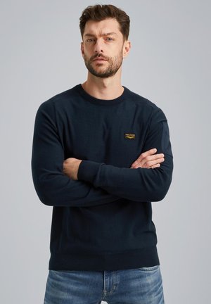 Maritieme crewneck trui van een zachte brei met ribgebreide manchetten en zoom. Bevat een klein merklabel op de borst. Gedirigeerd met lichtblauwe spijkerbroek.