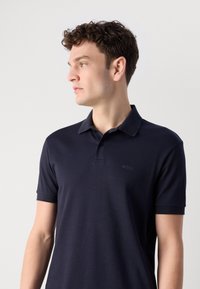 Jūros laivyno polo marškiniai, trumpomis rankovėmis, minkšta medžiaga, trijų mygtukų apykaklė, su subtiliu ženklu "BOSS" kairėje krūtinės pusėje.