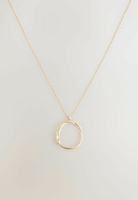 Gouden ketting met een ronde hanger versierd met kleine heldere stenen aan één kant, hangend aan een delicate ketting.