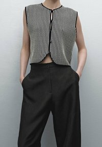 Svart och vit randig stickad ärmlös topp med knappstängning och rundad nederkant, tillsammans med avslappnade svarta byxor.