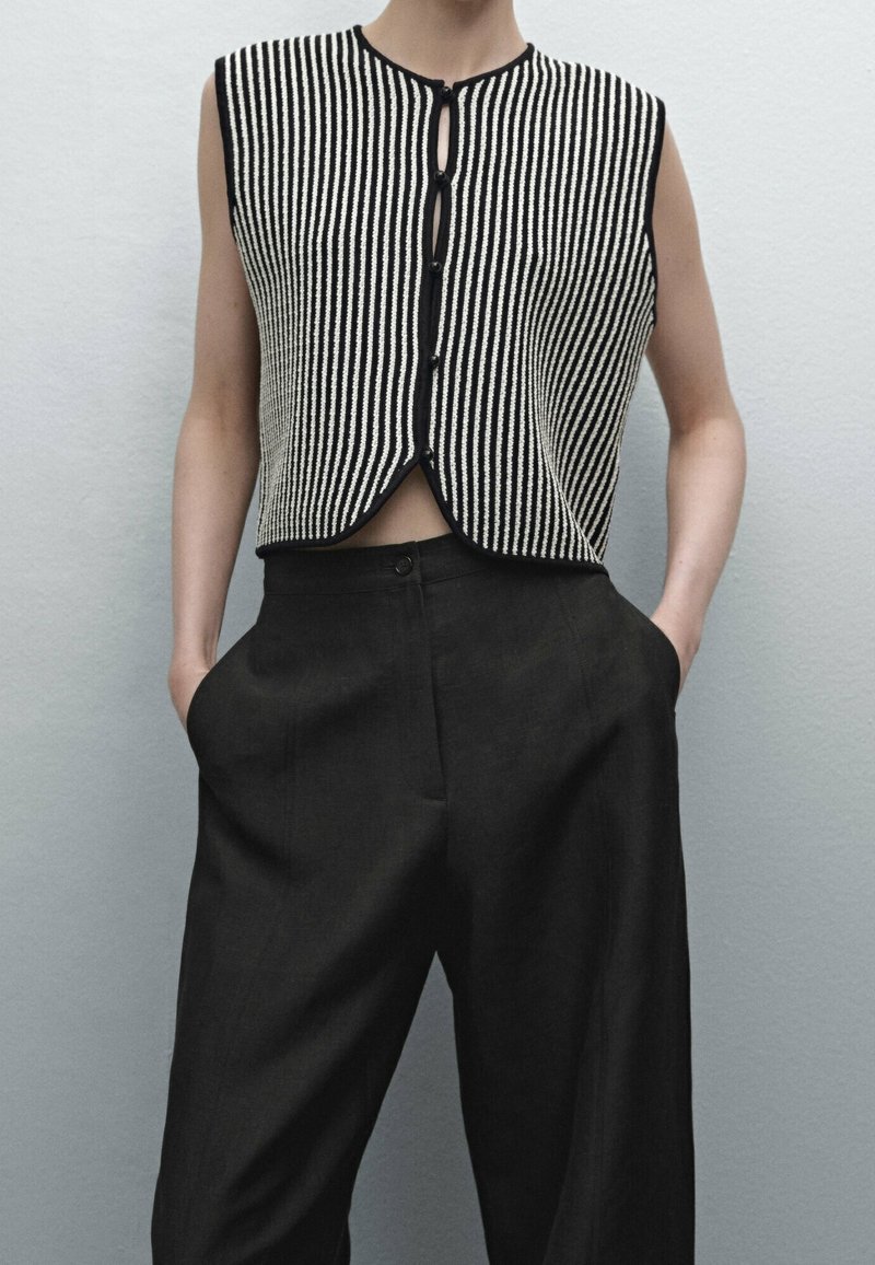 Svart och vit randig stickad ärmlös topp med knappstängning och rundad nederkant, tillsammans med avslappnade svarta byxor.