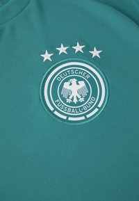 Grüner Stoff mit dem Emblem des Deutschen Fußball-Bundes, das einen weißen Adler und vier Sterne darüber zeigt, darauf gestickt.