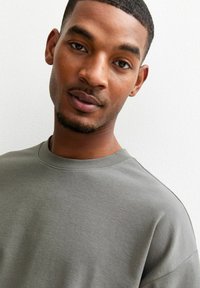 Grå t-shirt med rund halsringning, tillverkad av mjukt tyg, med korta ärmar och en avslappnad passform. Texturen är slät, med en enkel design.