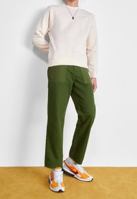 Světlé béžové mikina s žebrovanými manžetami, zelené cargo kalhoty s volným střihem a tenisky v kombinaci barev s oranžovými akcenty.