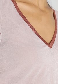 Lys pink V-hals top med en glitrende tekstur og bronze kant langs halsudskæringen. Stoffet er glat og tætsiddende omkring den øvre del af torsoen.