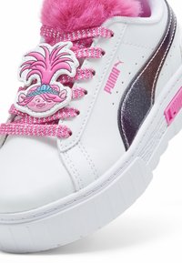 Bílá teniska s růžovými chlupatými doplňky, kovovým bočním pruhem a šněrovadly s potiskem, na jazyku je barevná postavička.