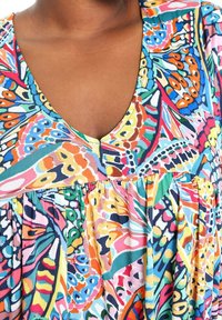 Tunique colorée et à motifs avec un décolleté en V profond. Présente un col froncé et une texture de tissu fluide dans diverses teintes.