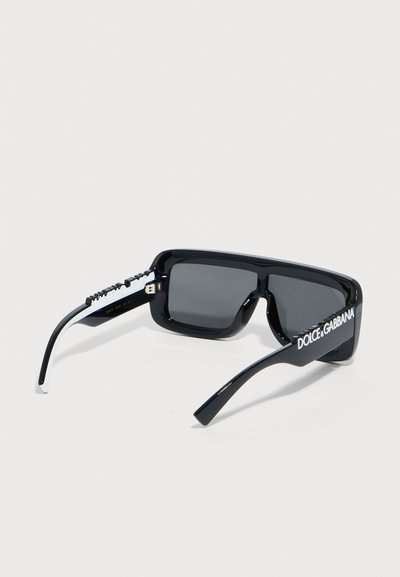 Μαύρα ορθογώνια γυαλιά ηλίου με σκουρόχρωμους φακούς και λευκό λογότυπο "Dolce & Gabbana" στα πλαϊνά μπράτσα, σε φωτεινό φόντο.