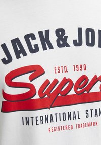 White t-shirt with bold black and red text reading "JACK & JONES Super" and "ESTD 1990" with a smooth cotton texture.