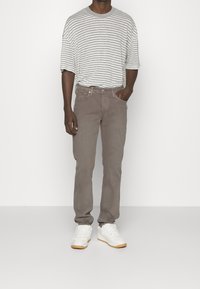 Šedé pruhované tričko s krátkými rukávy, kombinované s hnědými džíny z denimu. Obuv tvoří bílé tenisky s texturovaným designem a gumovou podrážkou.