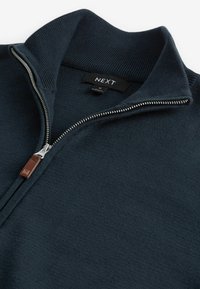 Pull tricoté bleu marine à fermeture éclair quart-de-zip avec col montant côtelé, fermeture éclair argentée, tirette en cuir et étiquette de la marque "NEXT" à l'intérieur du col.