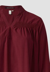 Bordeaux lange mouwen blouse met een V-hals en geplooide details over de borst. Gemaakt van zachte stof met een gladde textuur.