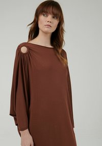 Vestido marrón, de tejido suave, con un amplio escote barco, mangas recogidas con abertura circular, ajuste holgado, cae suavemente hasta el dobladillo.