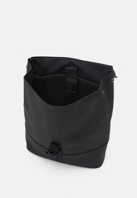 Black tote bag made of soft, textured material. Features a wide opening, a central strap closure, and interior pockets for organization.