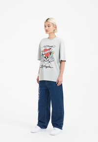 Gray oversized t-shirt with a graphic design featuring a skull and hearts, paired with blue wide-leg jeans and white sneakers.