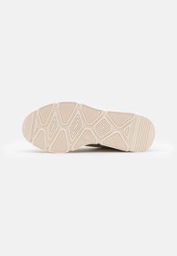 Sole di sneaker con una superficie in gomma beige testurizzata, caratterizzata da motivi geometrici e scanalature per la trazione, un tallone liscio e una punta arrotondata.