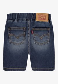 Shorts en denim avec une teinte bleu foncé, taille élastique, deux poches arrière avec coutures jaunes et une étiquette en cuir marron à la taille.