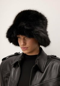 Čierny kožený klobúk s širokým, mäkkým okrajom a textúrovaným povrchom, nosený s čiernou koženou bundou so zipsom a ramennými detailmi.