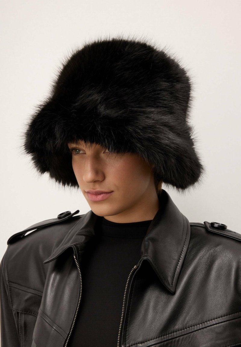 Čierny kožený klobúk s širokým, mäkkým okrajom a textúrovaným povrchom, nosený s čiernou koženou bundou so zipsom a ramennými detailmi.