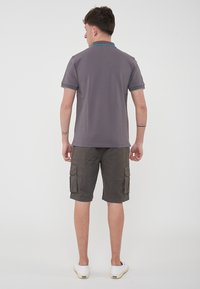 Polo grigio con colletto blu e verde, abbinato a pantaloni cargo scuri con quattro tasche e sneakers bianche.