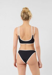 Completo bikini nero con sottili spalline bianche, caratterizzato da una schiena a scoop e un bordo bianco a contrasto su entrambi i pannelli, superiore e inferiore.