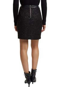 Svart, paljetterad minikjol med en figurnära design och midja i läder. Har en dragkedja bak och texturerad tyg. Matchas med svarta ankelskor.