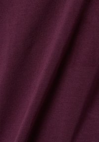 Tessuto bordeaux con una superficie liscia e una leggera elasticità, caratterizzato da un sottile motivo a coste e una distribuzione uniforme del colore.