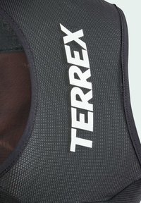 Schwarze Mesh-Sportweste mit dem auffällig platzierten weißen Text "TERREX". Strukturierter Stoff mit sichtbaren Nähten und Ausschnittdesign.