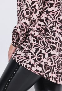 Top nero e rosa a fantasia con un design floreale e motivi a fiocco, abbinato a leggings neri lucidi decorati con borchie.