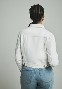 Valge denim jakk kontrastsete kollaste õmblustega, figuuriuhendav disain ja metallnupud, koos helesiniste kõrge talje ning teksapükstega.
