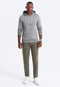 Grauer Hoodie mit Kängurutasche, verstellbaren Kordeln und gerippten Bündchen. Olivgrüne Hose im schlanken Schnitt, mit Seitentag. Weiße Sneakers.