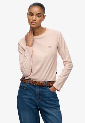 Lyserød langærmet t-shirt med rund halsudskæring og let raglanærmer. Har et lille broderet logo på brystet og casual jeans.