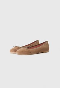 Ballerine in suede color marrone chiaro con punta arrotondata, dettaglio a fiocco sulla parte frontale e suola piatta. Il colore d'accento all'interno è un rosso a contrasto.