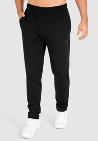 Zwarte sportbroek van zachte stof, met een elastische tailleband, zijzakken en een slim fit. Witte sneakers maken de look compleet.