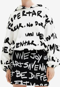 Felpa bianca con testo in stile graffiti nero, abbinata a una gonna nera con lettering a contrasto simile e design aderente.