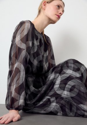 Robe noire transparente avec des motifs circulaires abstraits blancs, manches longues avec des poignets élastiques, col rond et silhouette fluide.
