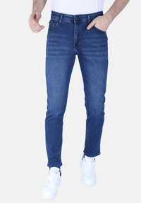 Skinny-fit donkerblauwe denim jeans met subtiele vervaging, vijf zakken, riemlussen en een knoopsluiting, gecombineerd met witte sneakers.