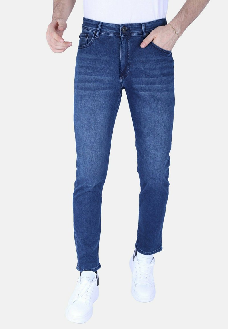 Skinny-fit donkerblauwe denim jeans met subtiele vervaging, vijf zakken, riemlussen en een knoopsluiting, gecombineerd met witte sneakers.